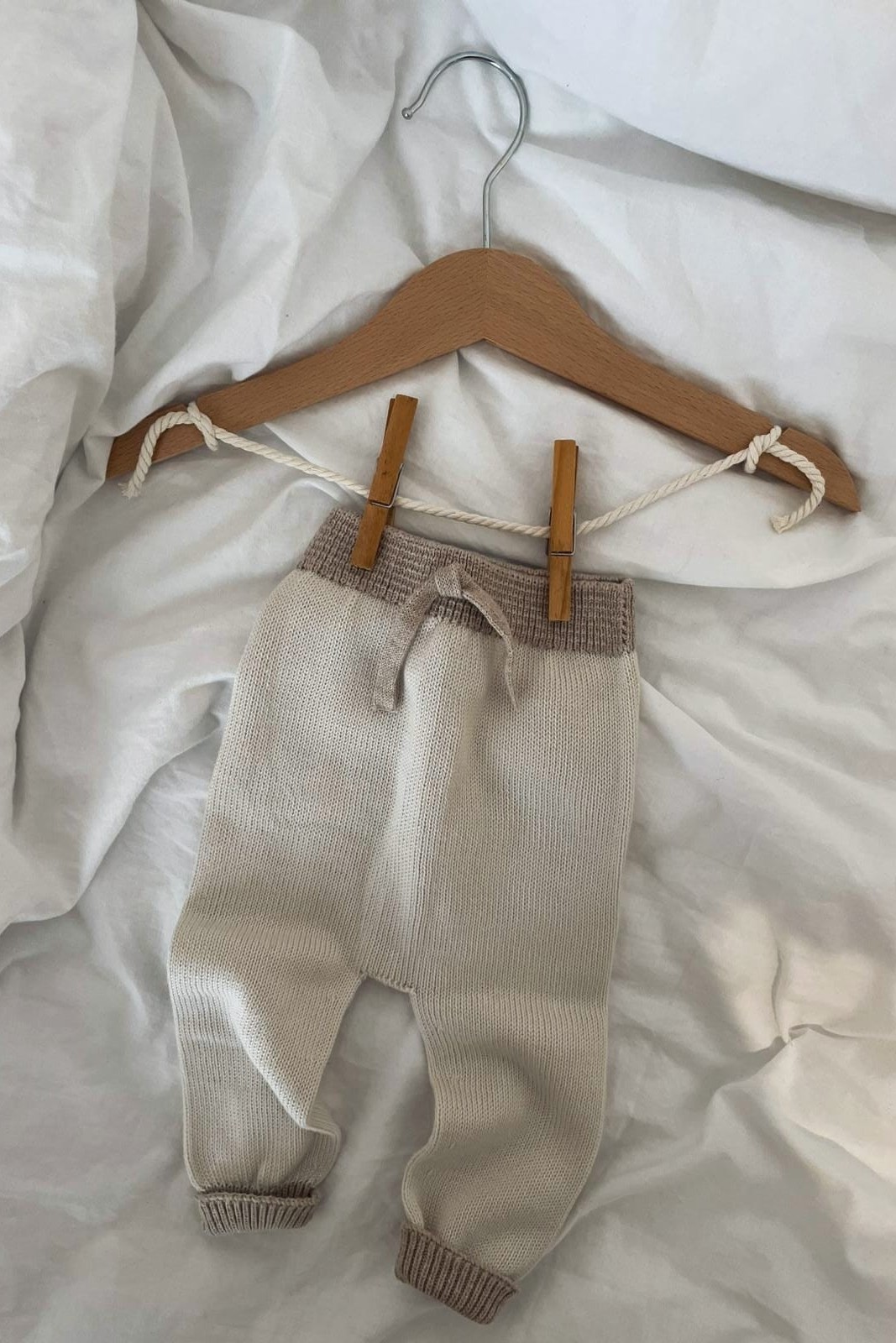 Calças de bebé bege em malha penduradas em cabide de madeira