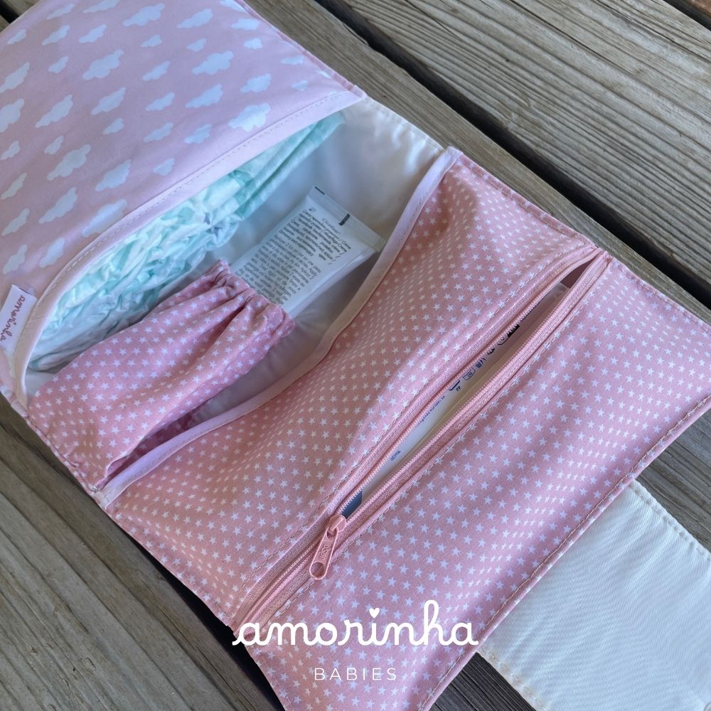 Organizador de fraldas rosa com estrelas brancas e bolsos, contendo fralda e tubo em superfície de madeira
