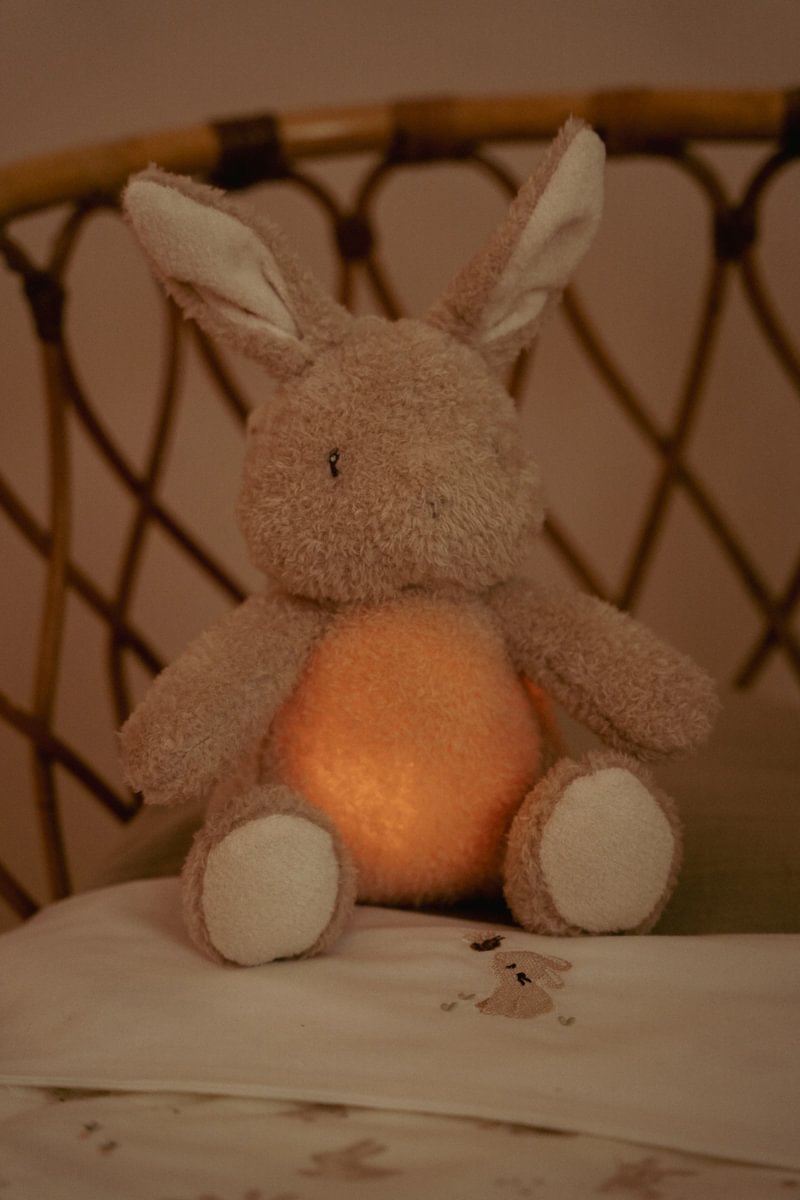 Ursinho de peluche castanho claro com barriga luminosa sentado na cama