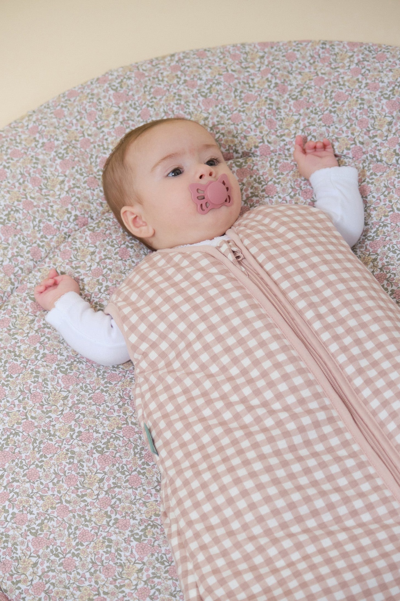 Bebé deitado num colchão com padrão floral e saco de dormir xadrez