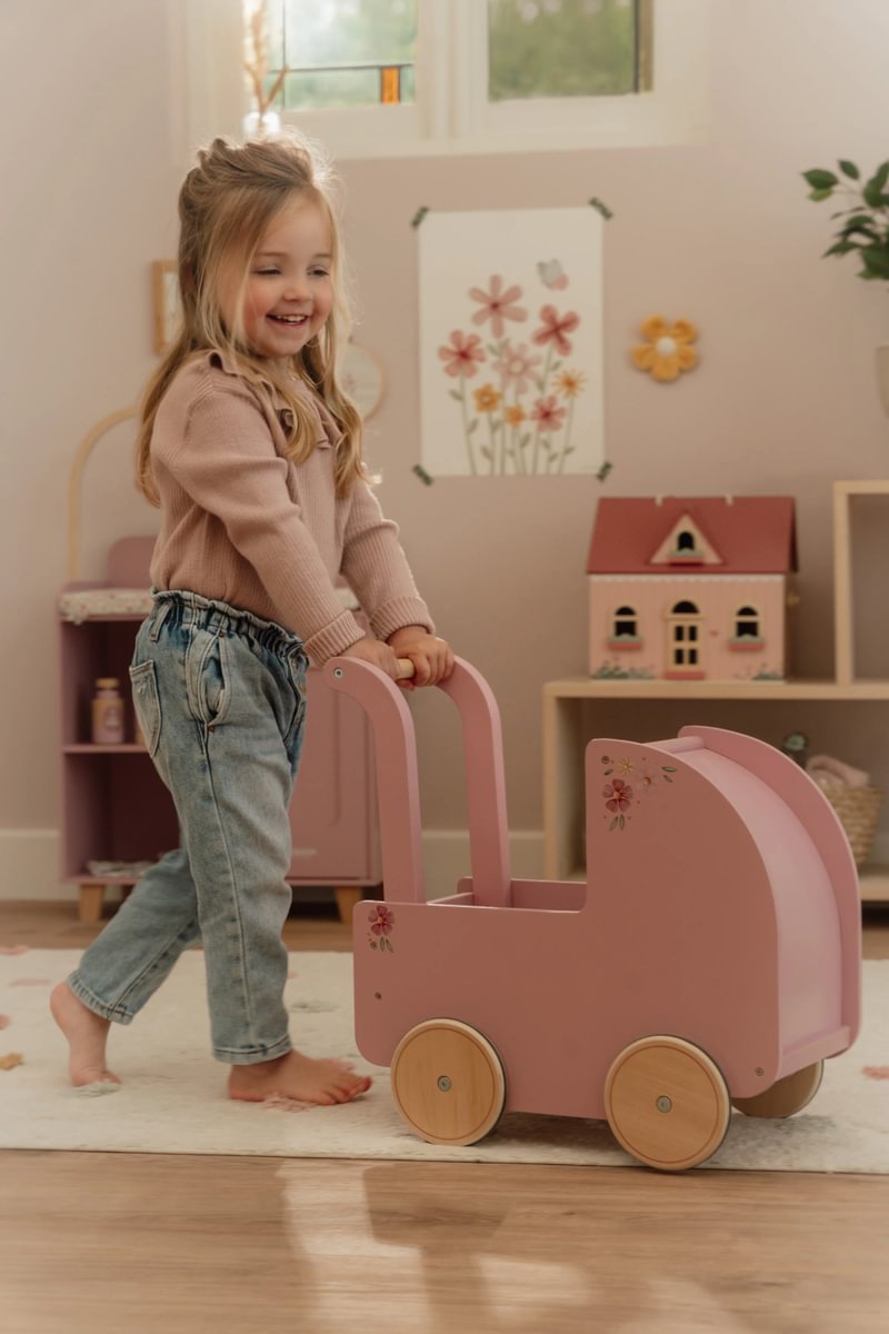 Criança com carrinho de brincar rosa em quarto decorado