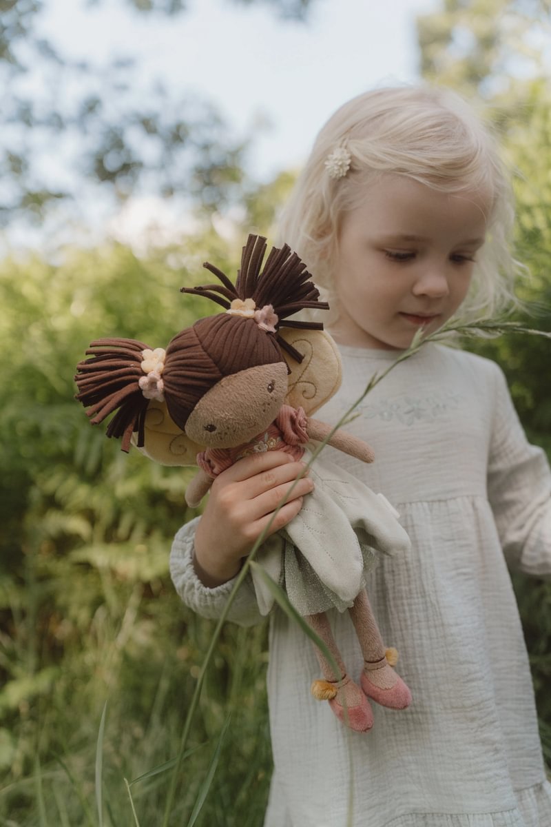 Criança segurando boneca fada de tecido com cabelo castanho e vestido cor-de-rosa em ambiente natural