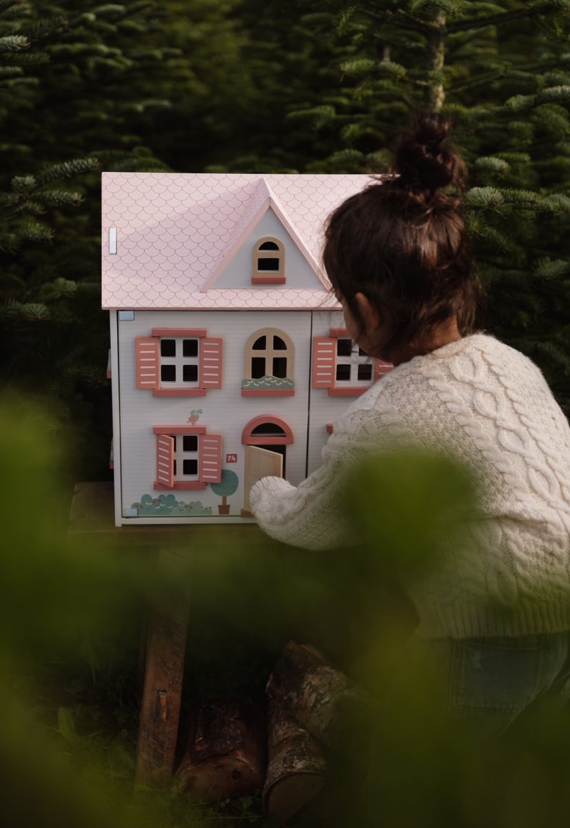 Casinha de brincar infantil de madeira com detalhes em rosa e uma criança a brincar em ambiente natural