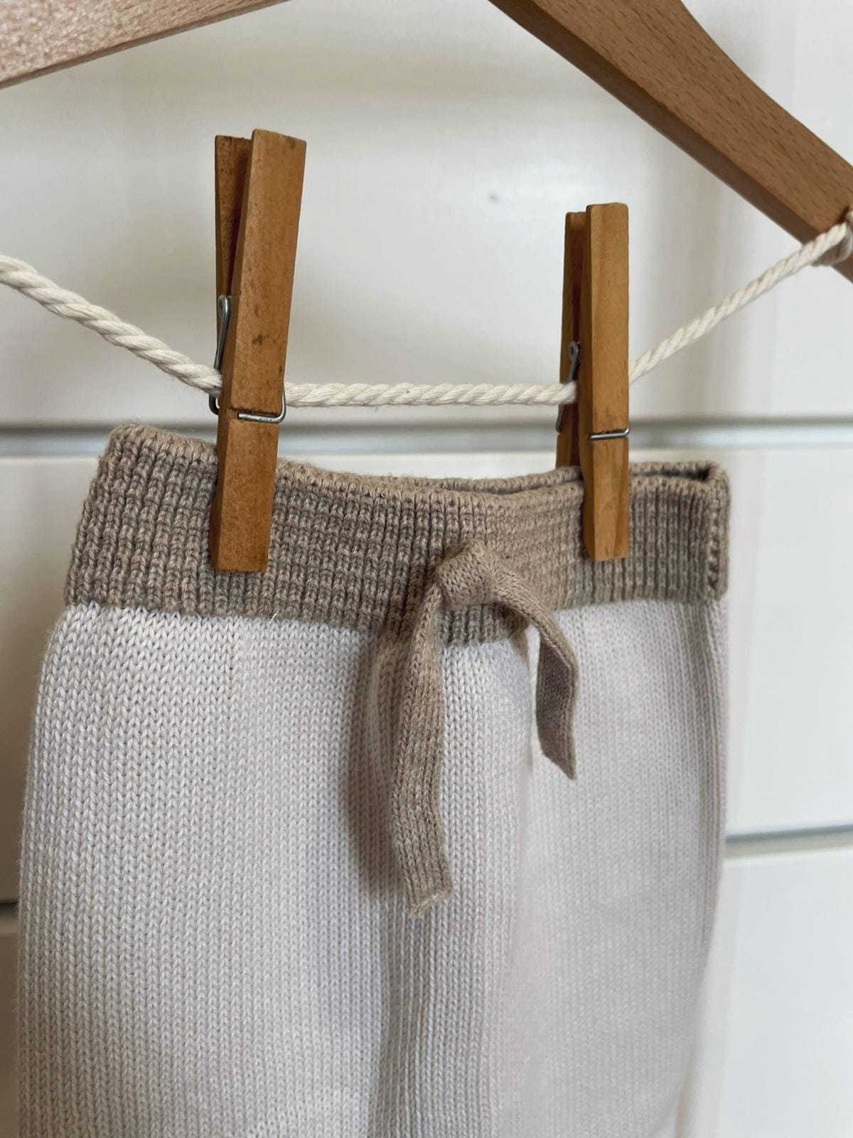 Peça de roupa branca e cinzenta pendurada num cabide de madeira