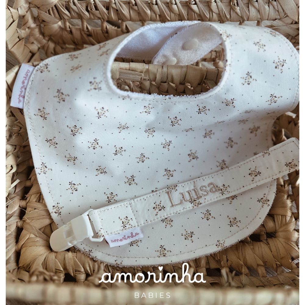 Babete e prendedor de biberão de tecido creme com pequenas flores castanhas.
