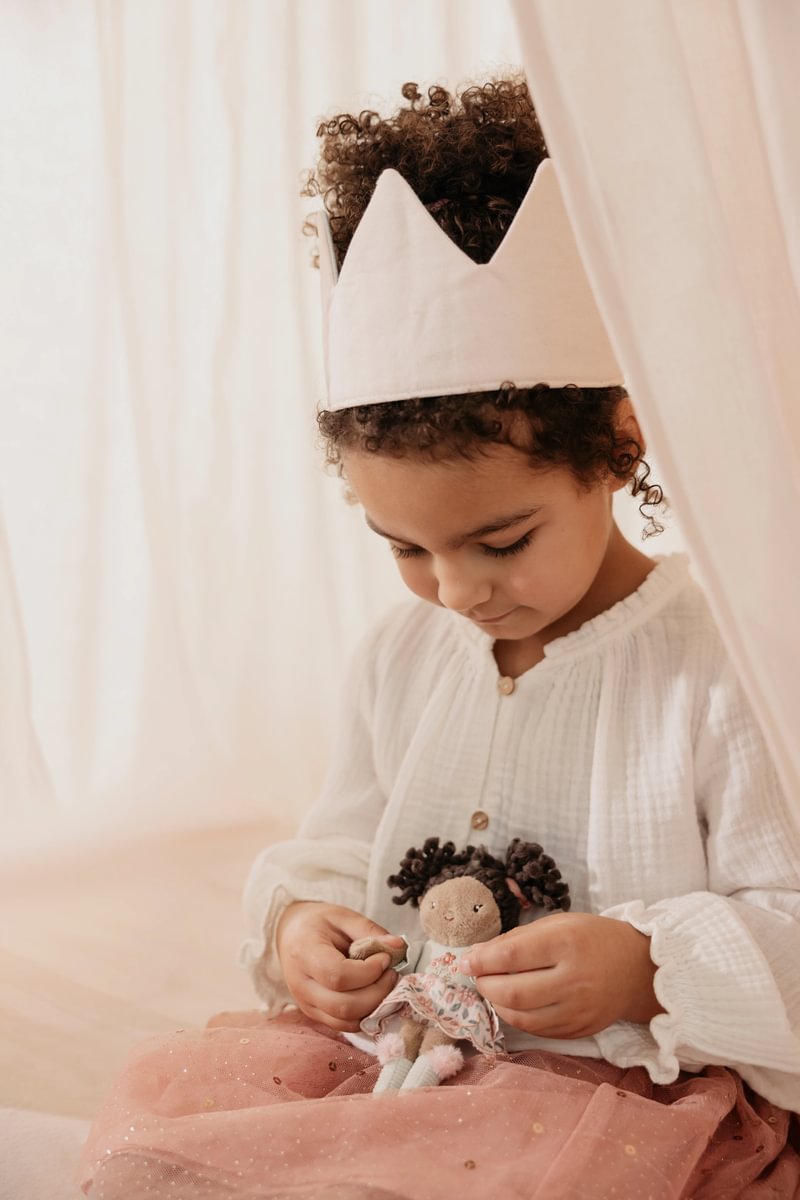 Criança com coroa branca segurando boneca de pano com vestido floral