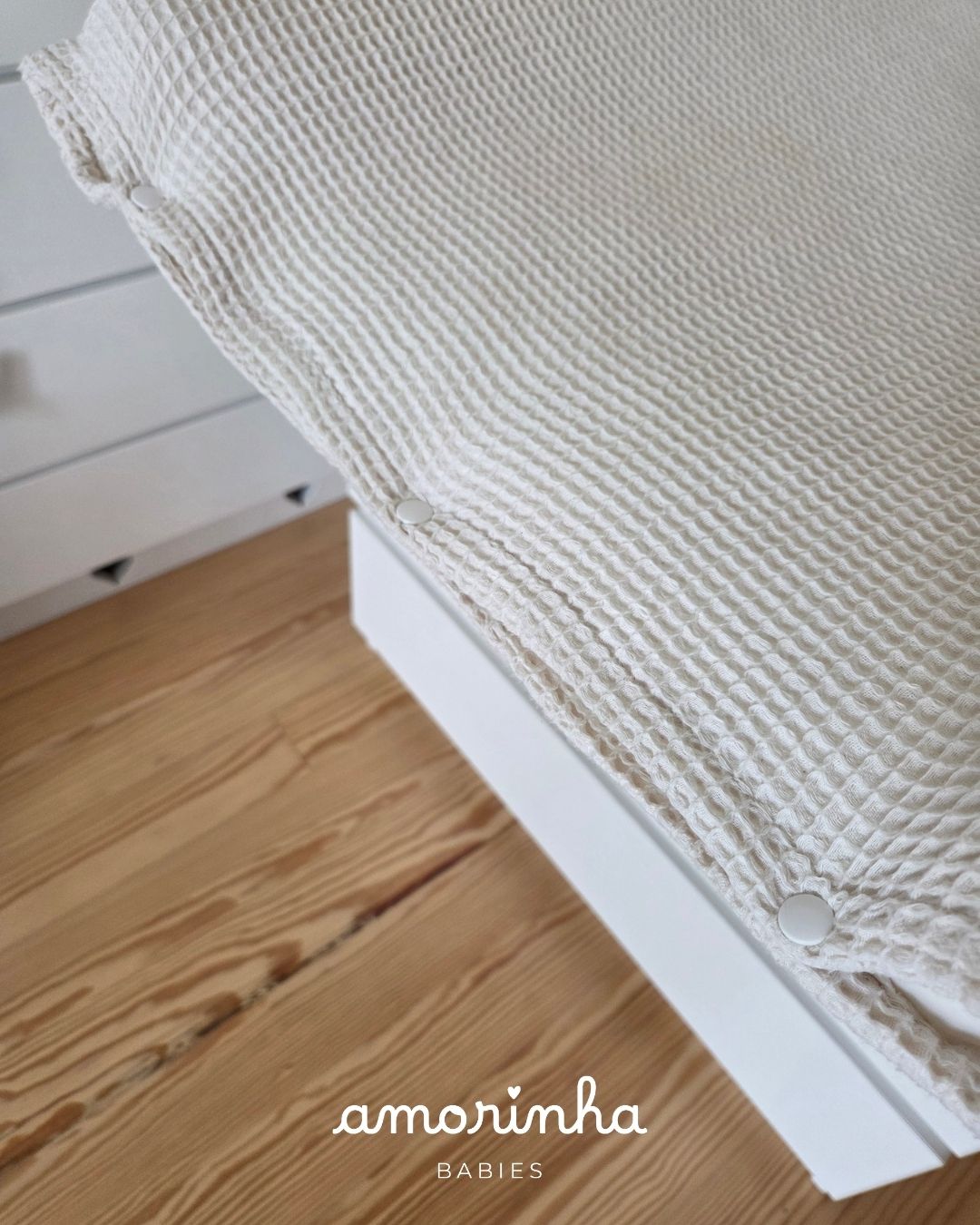 Manta creme texturizada com botões de pressão sobre superfície branca