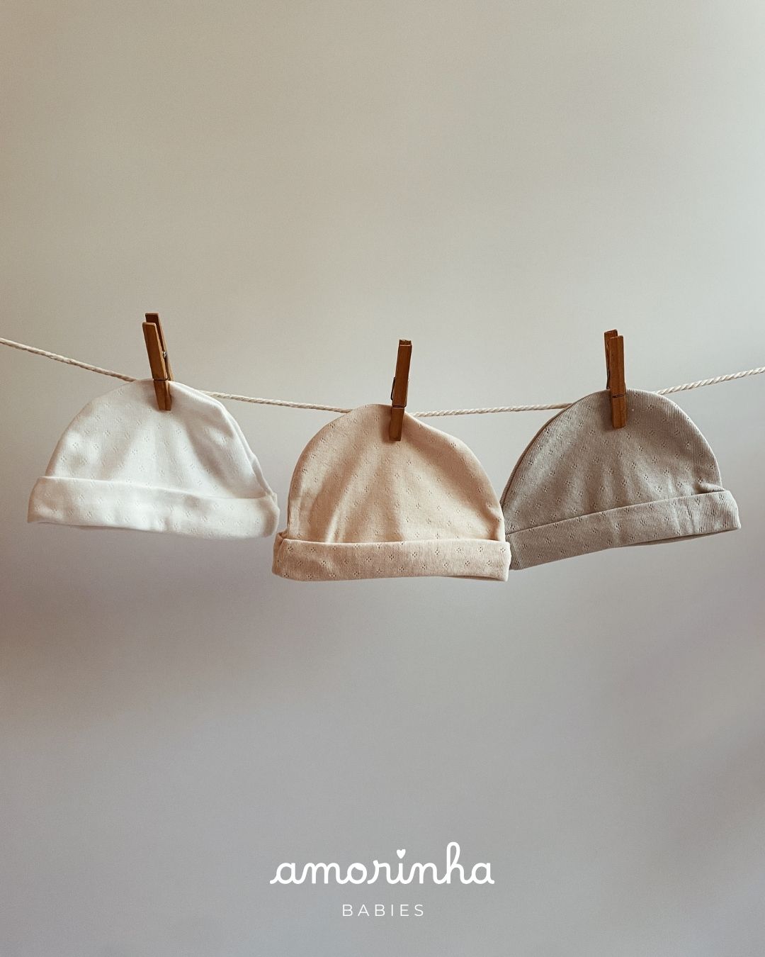 Três gorros de bebé em algodão pendurados em estendais com molas de madeira