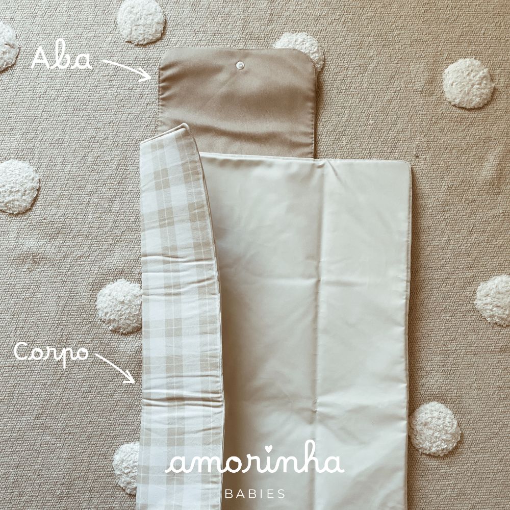 Capa bege com padrão xadrez e abas sobre tapete bege com pompons