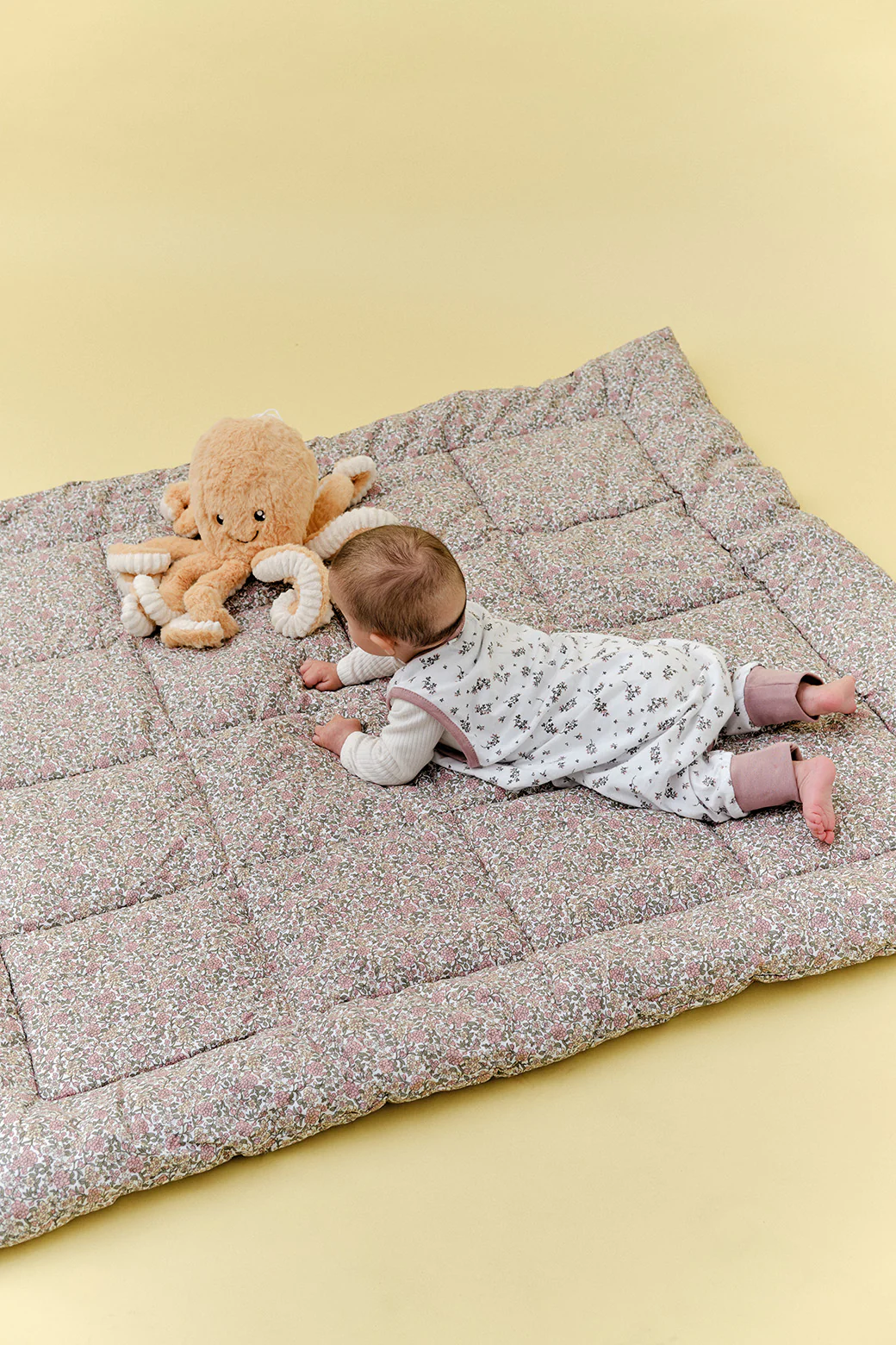 Bebé deitado em tapete acolchoado floral com peluche polvo