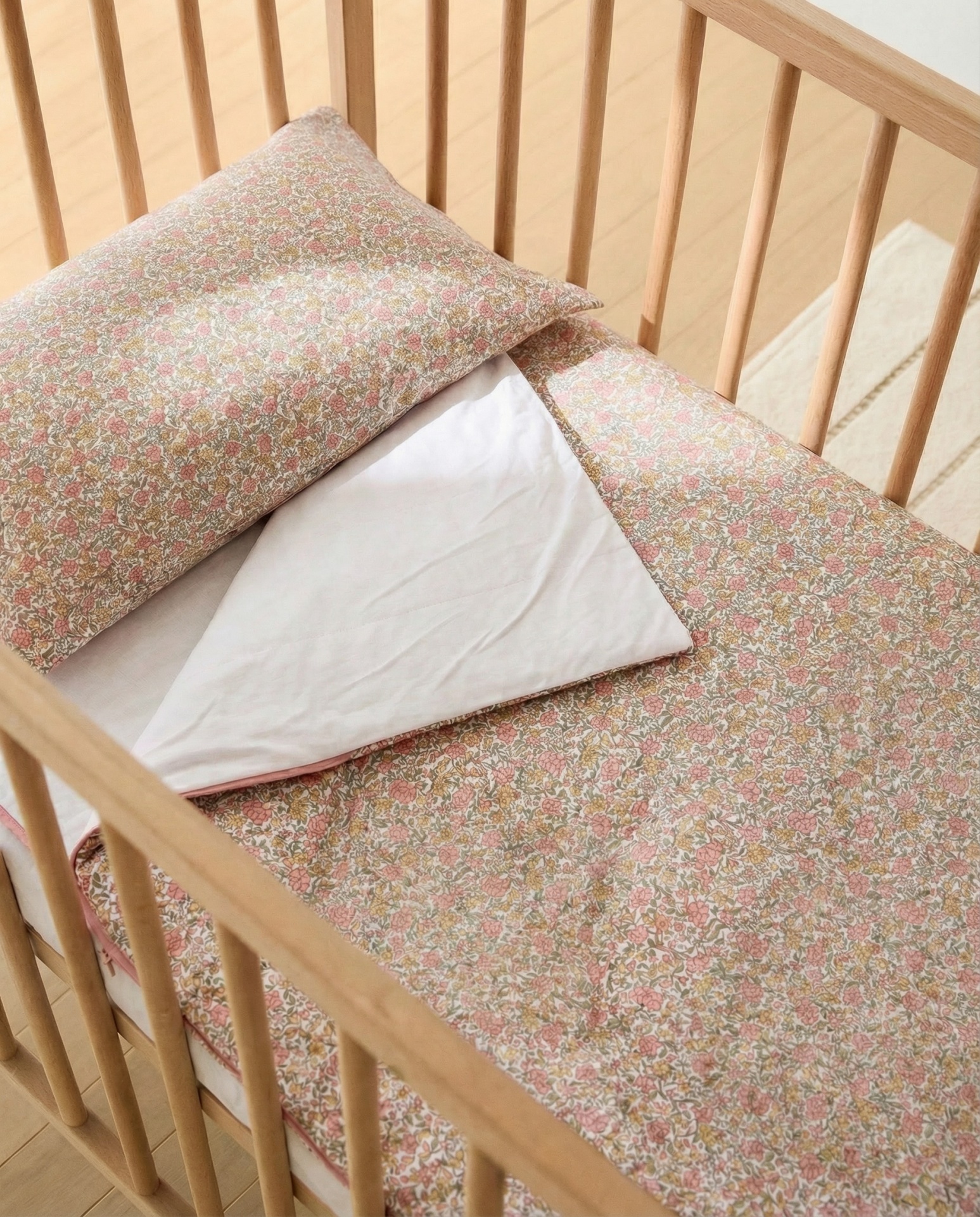 Berço de madeira com almofada e edredão floral colorido e lençol branco
