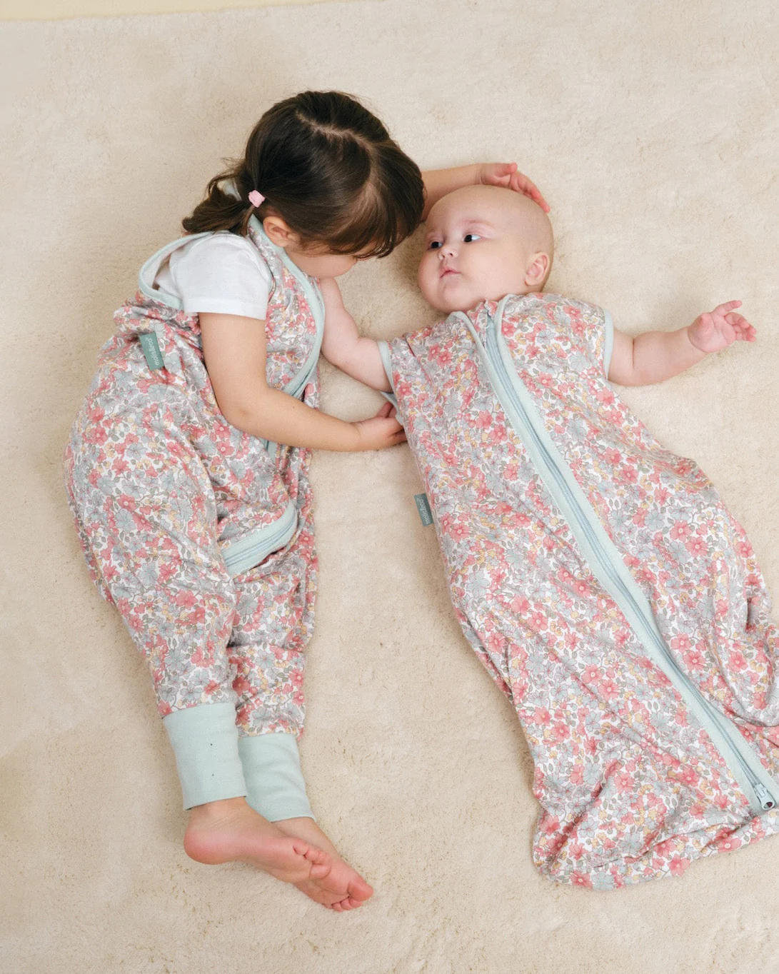 Bebés com sacos de dormir florais em tapete bege claro