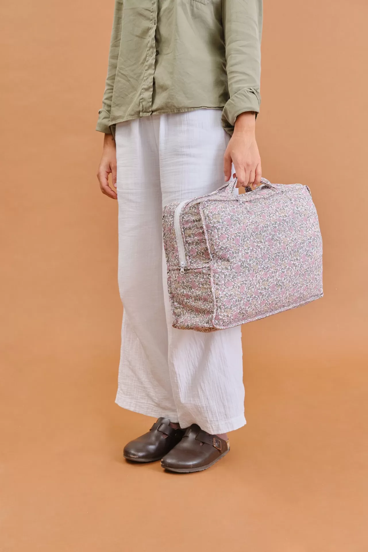 Mala floral em tecido com padrão rosa e verde segurada por pessoa com roupa verde e branca