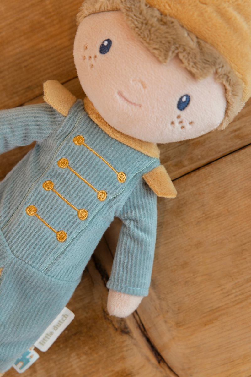 Boneco de peluche com roupa azul e detalhes amarelos sobre fundo de madeira