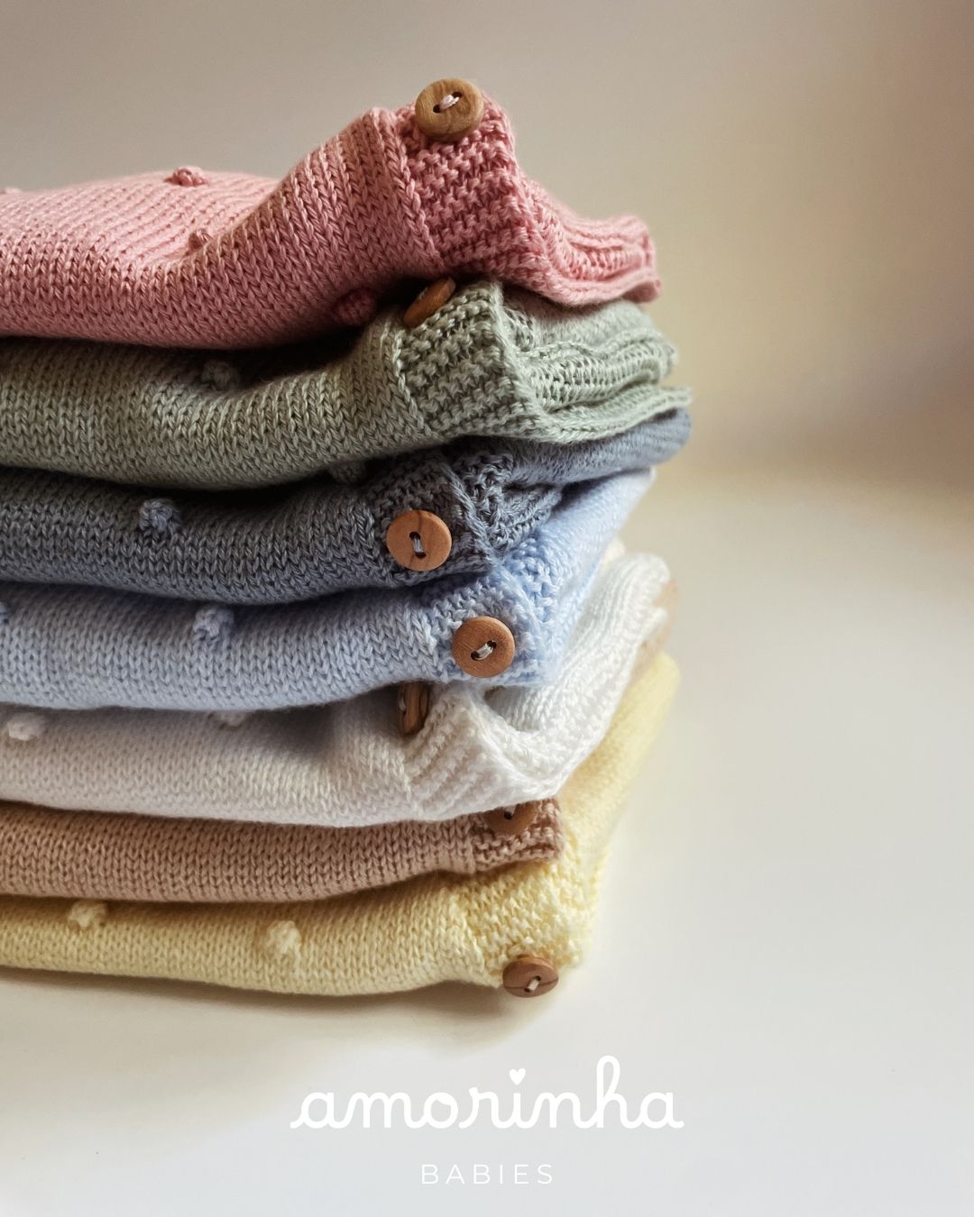 Peças de roupa de bebé em malha colorida com botões de madeira.