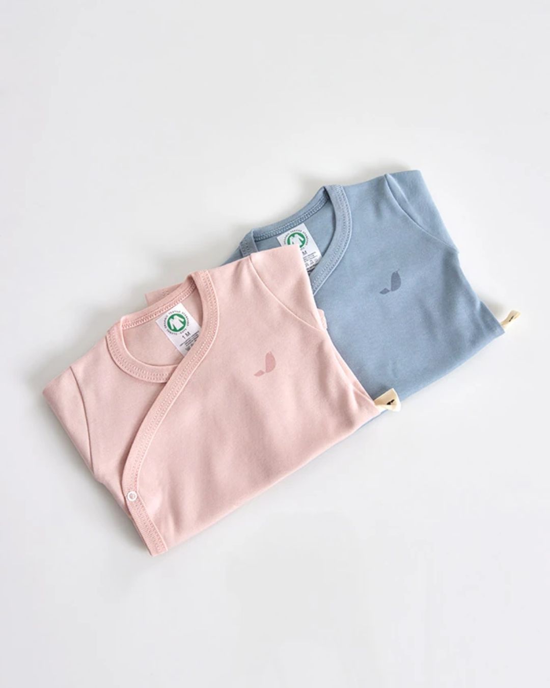 Dois bodies de bebé rosa e azul dobrados em fundo branco.