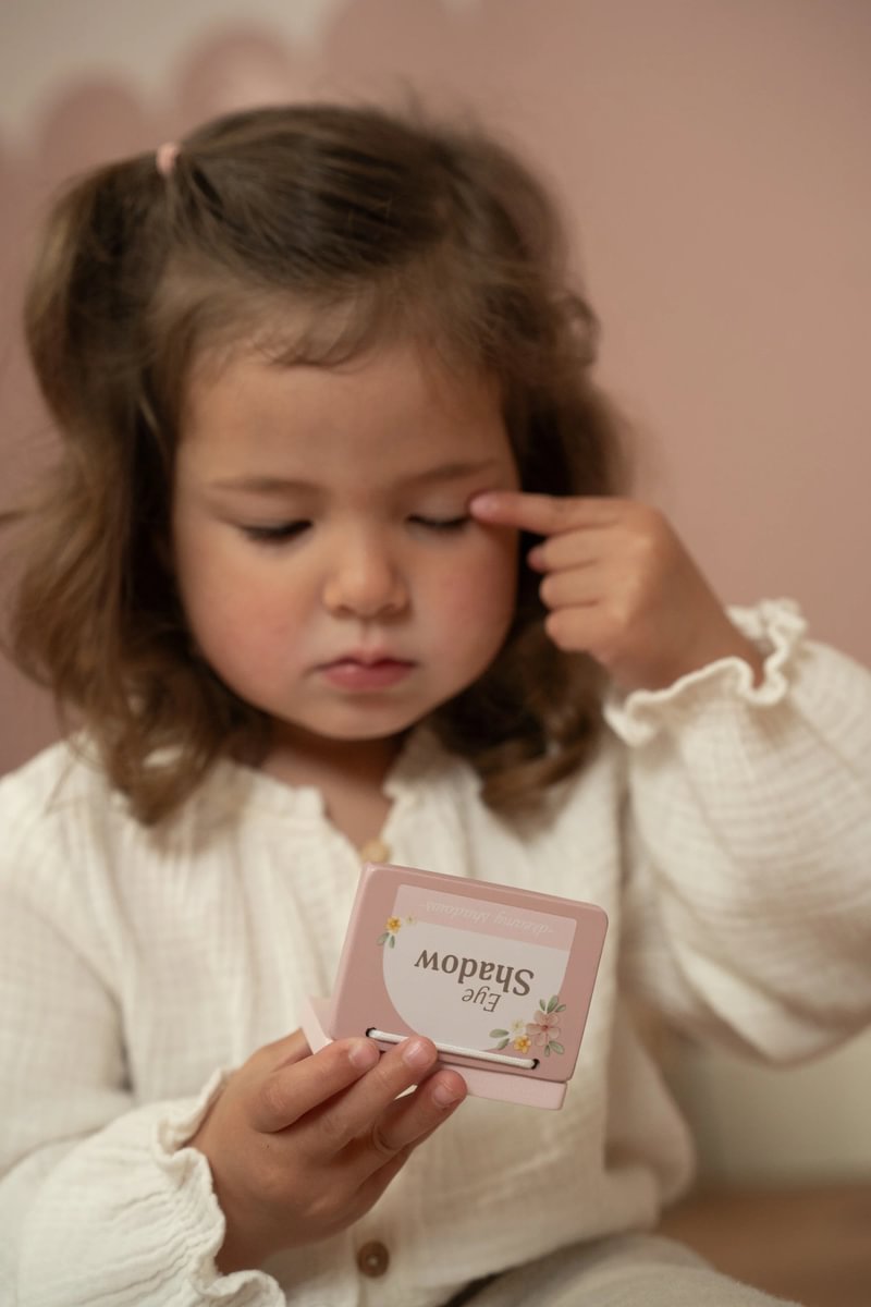 Criança segurando estojo rosa de sombra de olhos com decoração floral.