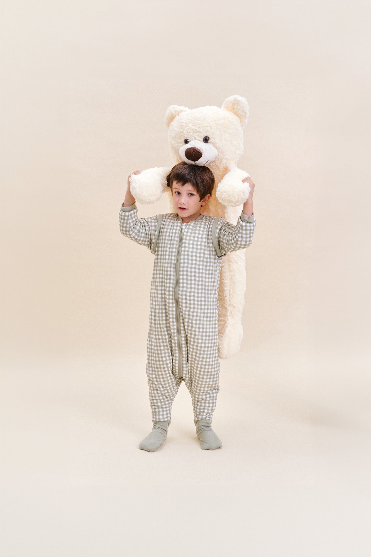 Menino com pijama xadrez segurando urso de pelúcia creme