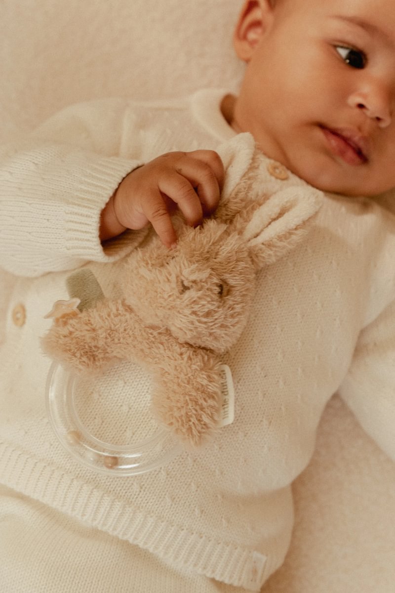 Bebé de camisola branca segurando brinquedo de peluche castanho claro em forma de coelho.