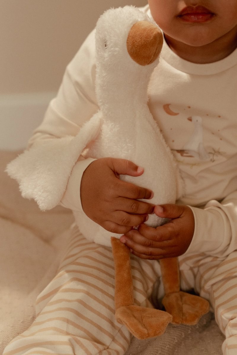 Pelúcia de ganso branco e castanho nas mãos de uma criança com pijama às riscas e t-shirt clara.