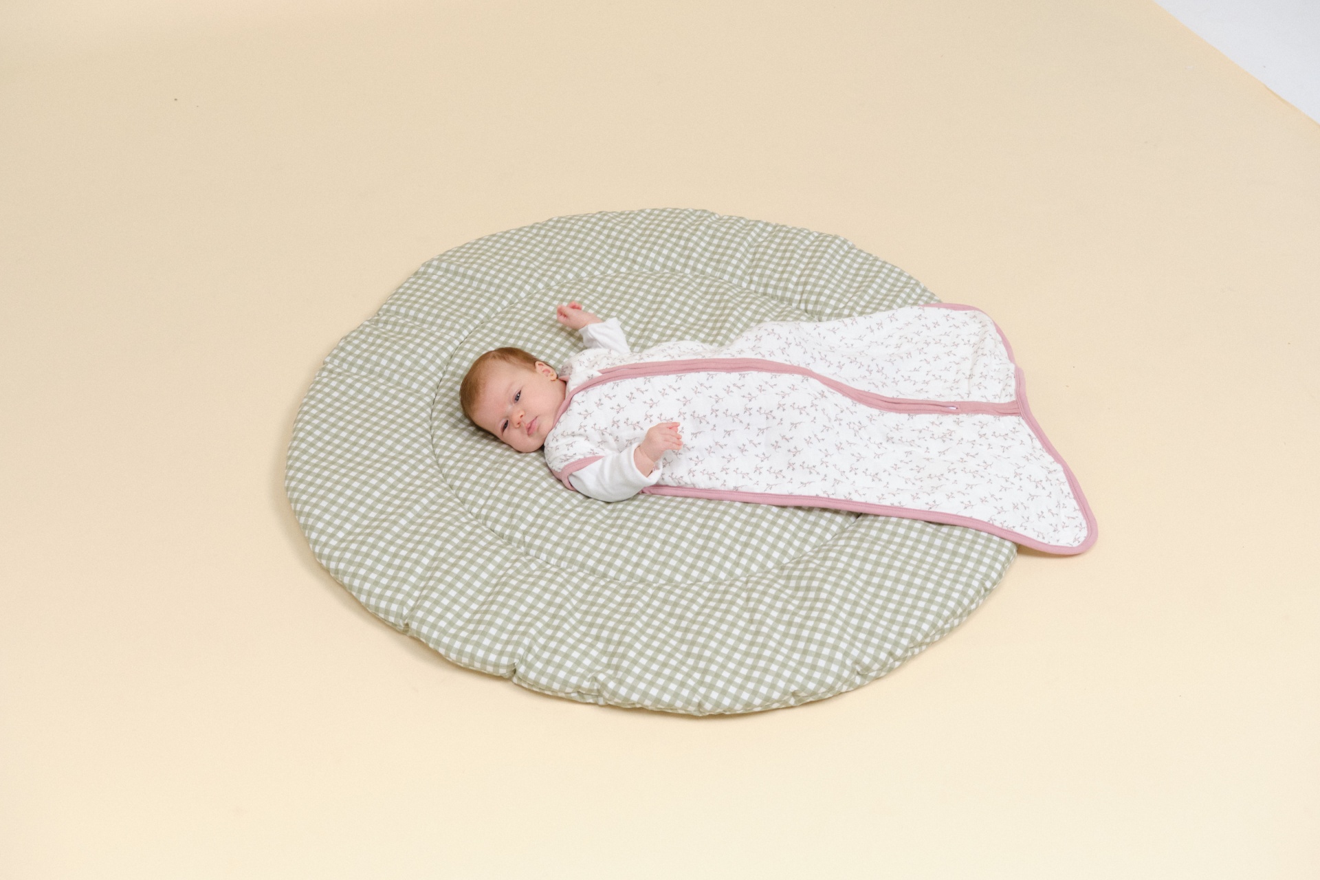 Bebé deitado em saco de dormir floral sobre almofada circular cinza clara