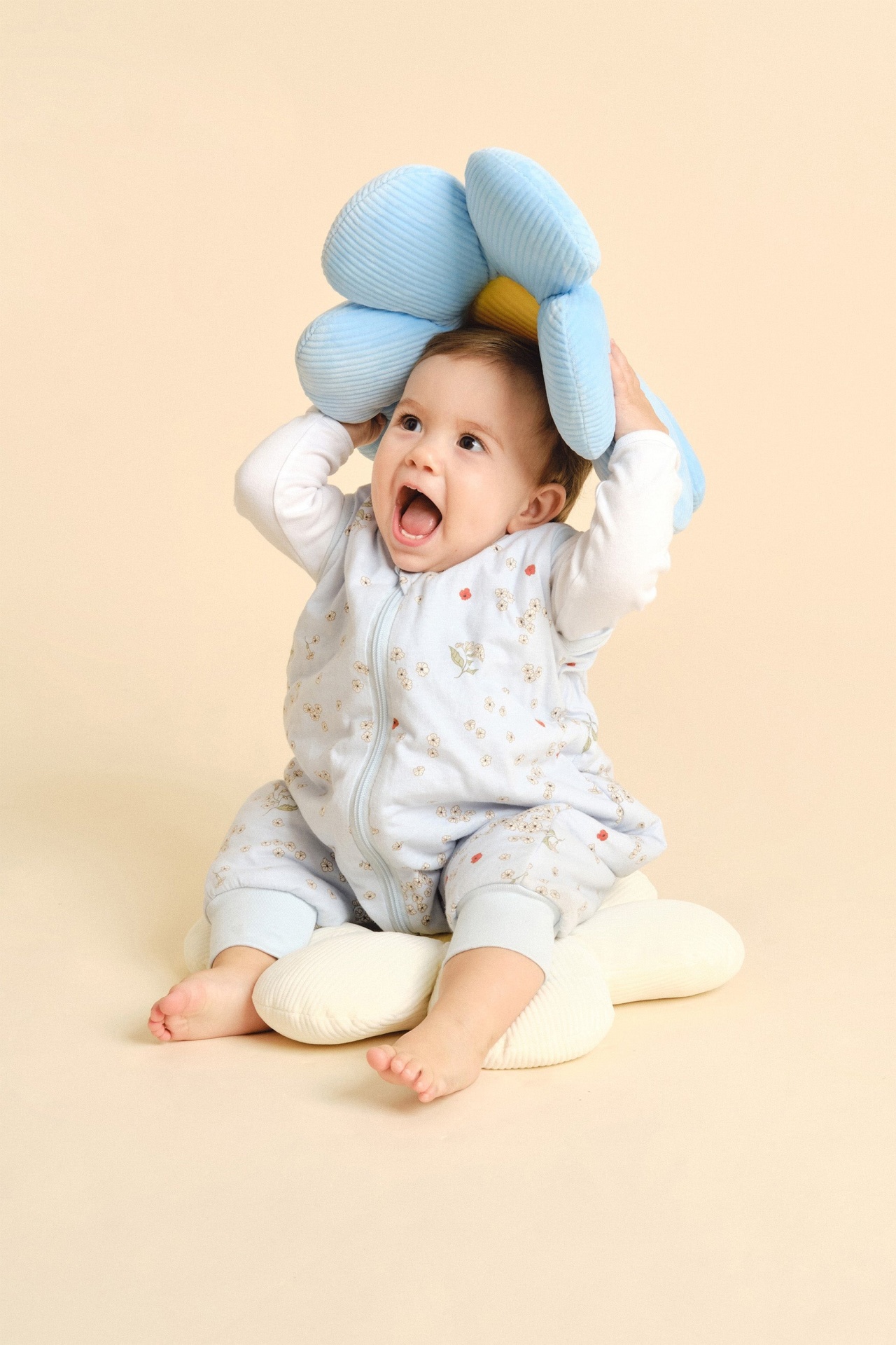 Bebé com pijama floral e almofada em forma de flor azul e amarelo
