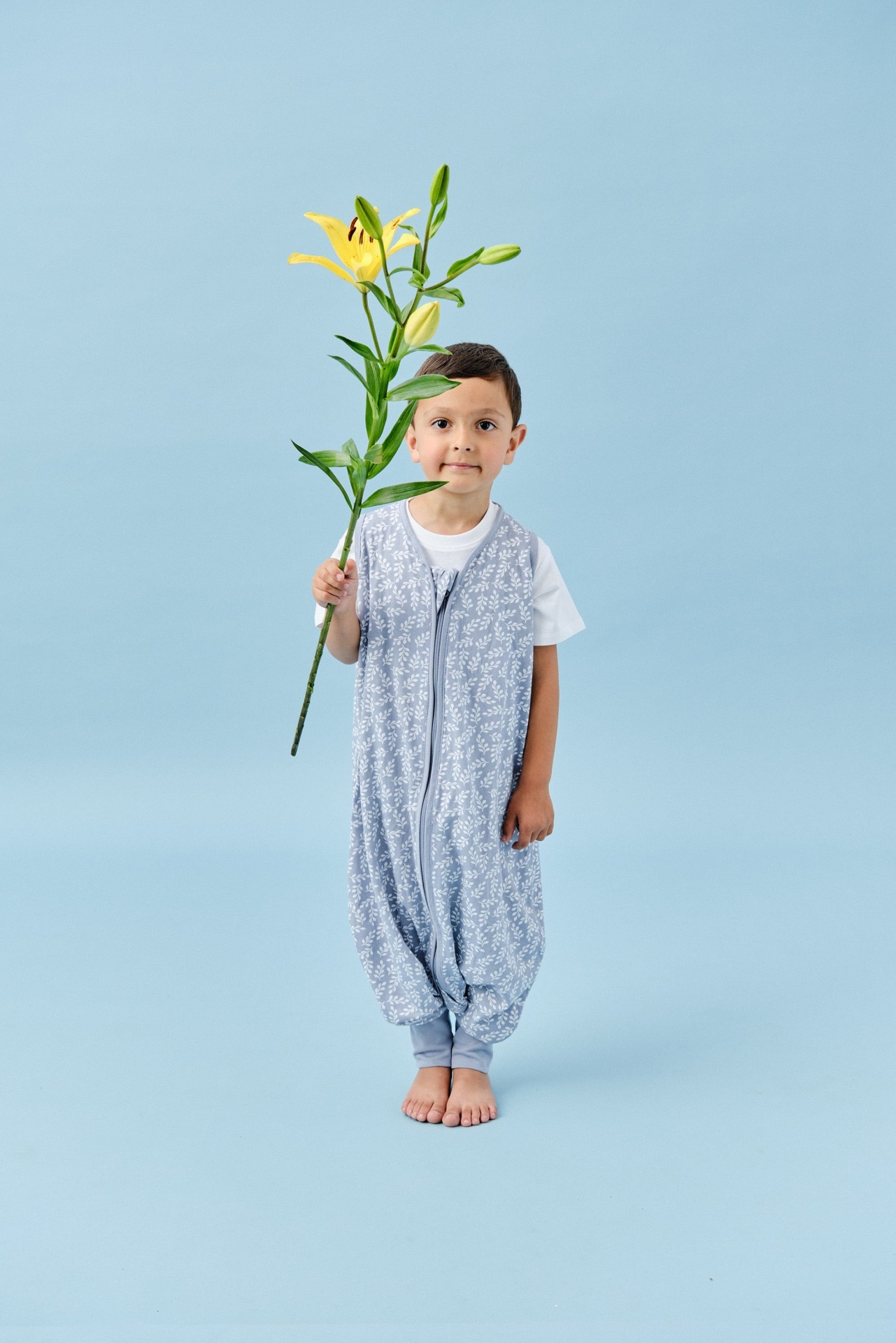 Criança com saco de dormir azul com padrão branco segurando flor amarela gigante