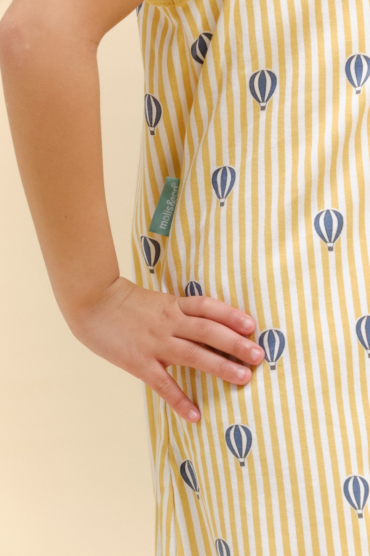 Roupa infantil com padrão de riscas amarelas e balões azuis, etiqueta verde molis&co®