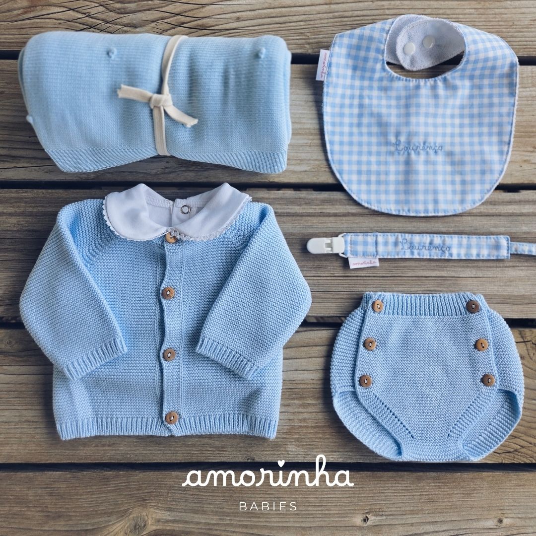 Conjunto de roupa e acessórios de bebé em tons de azul claro sobre madeira