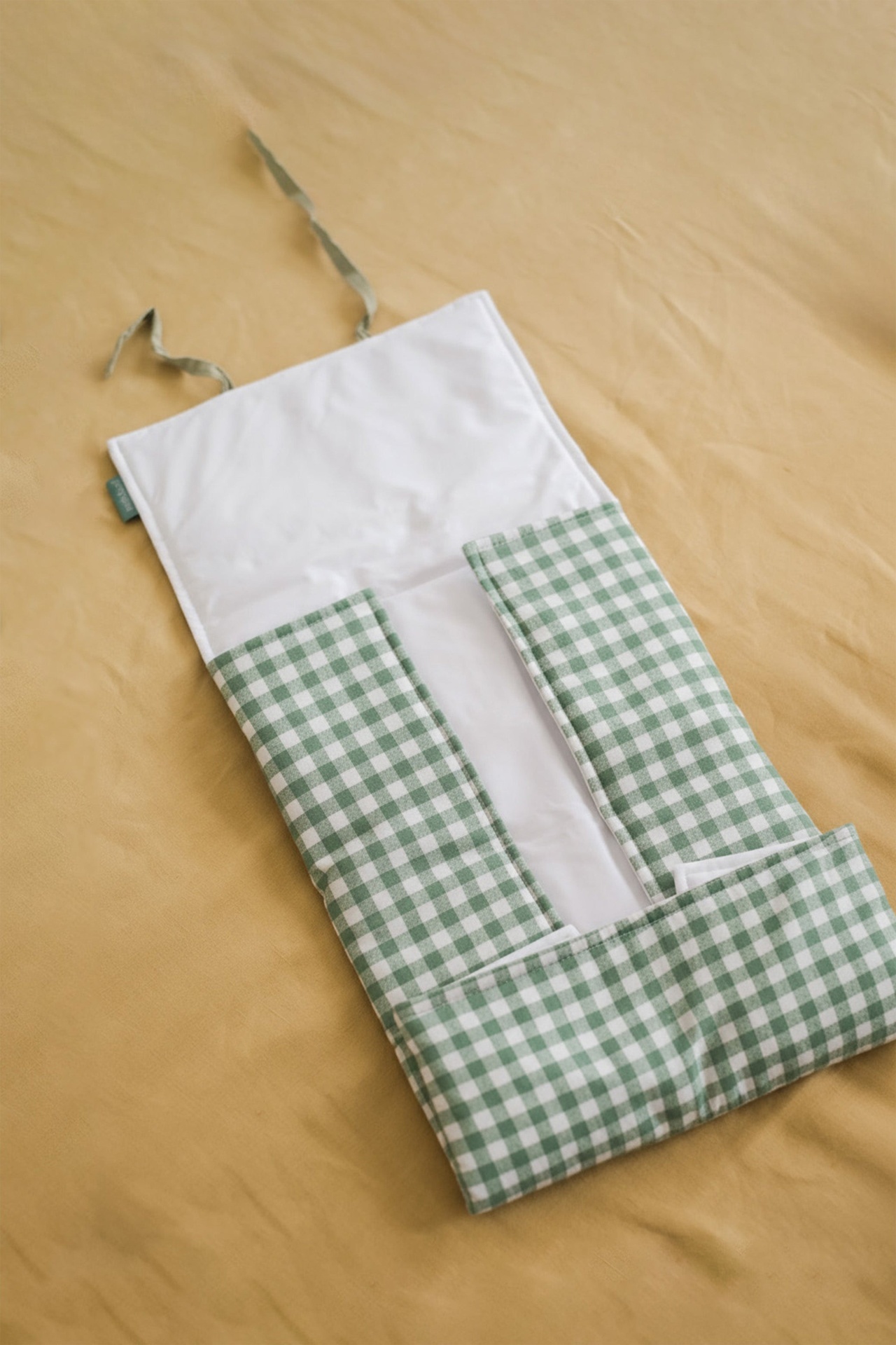 Organizador de talheres de pano xadrez verde e branco com bolsos e alças sobre tecido amarelo