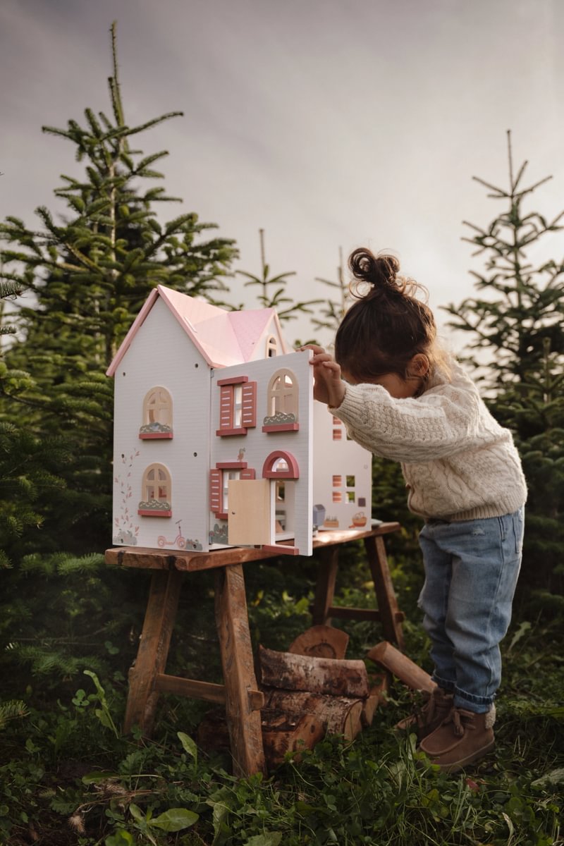 Boneca de casa de madeira branca e rosa com criança a brincar no exterior