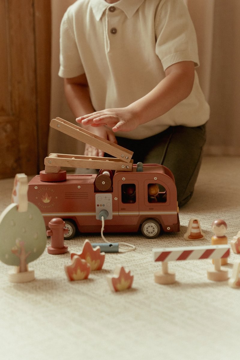 Brinquedo de carrinho de bombeiros de madeira com acessórios em madeira sobre tapete claro