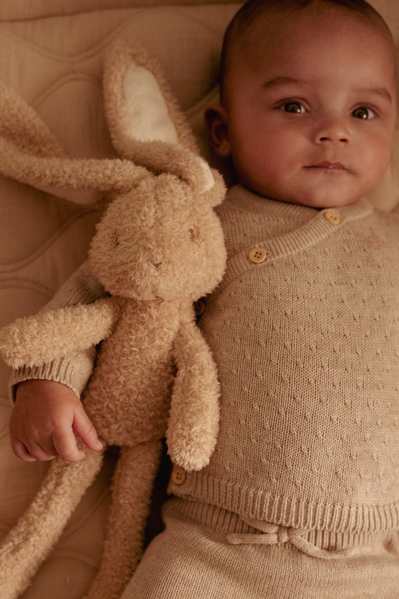 Bebé com roupa bege segurando coelho de pelúcia
