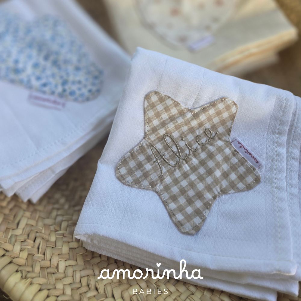 Fralda de bebê branca com aplicação em estrela xadrez bege e nome bordado Alice sobre superfície de palha