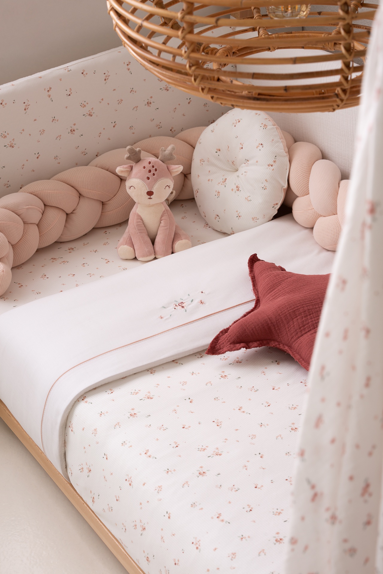 Berço de bebé com lençóis estampados, almofada redonda, protetor trançado, peluche veado cor-de-rosa e almofada estrela bordô