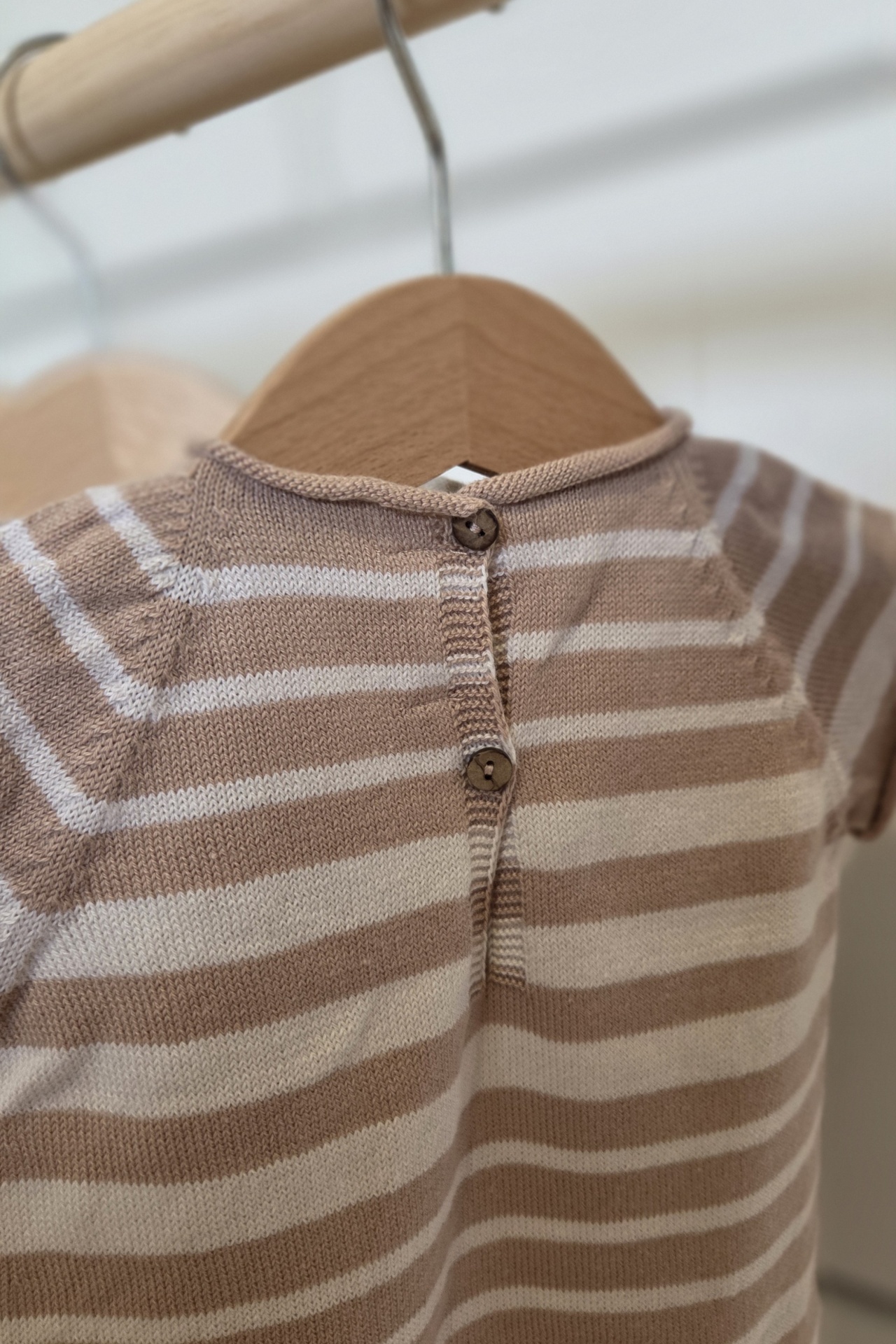 Camisola de bebé às riscas bege e branco com botões pendurada num cabide.