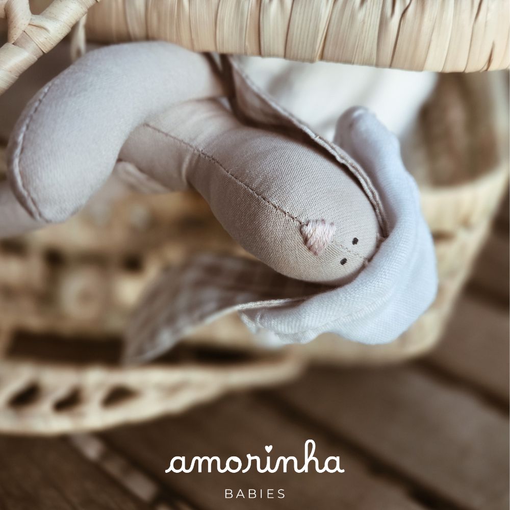 Boneco de peluche bege e branco com detalhes rosas sobre madeira e cadeira de vime