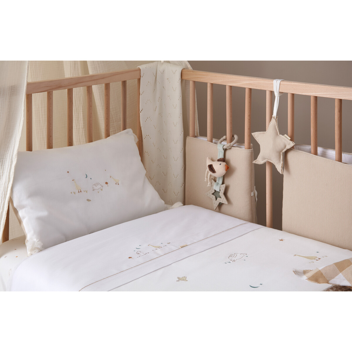 Berço de madeira com roupa de cama branca decorada e protetores em tecido bege