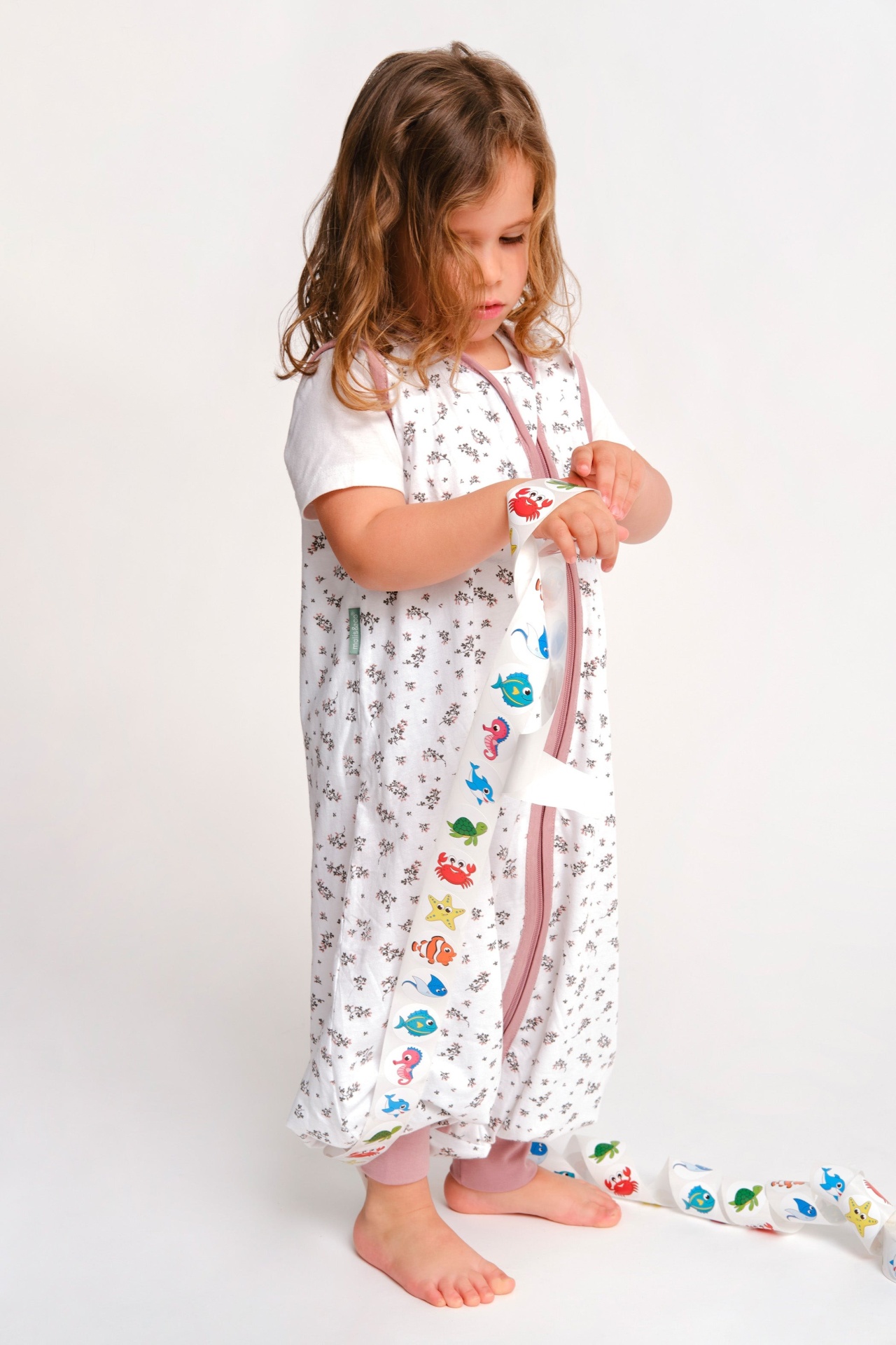 Criança com saco de dormir floral branco e fita com desenhos de animais marinhos
