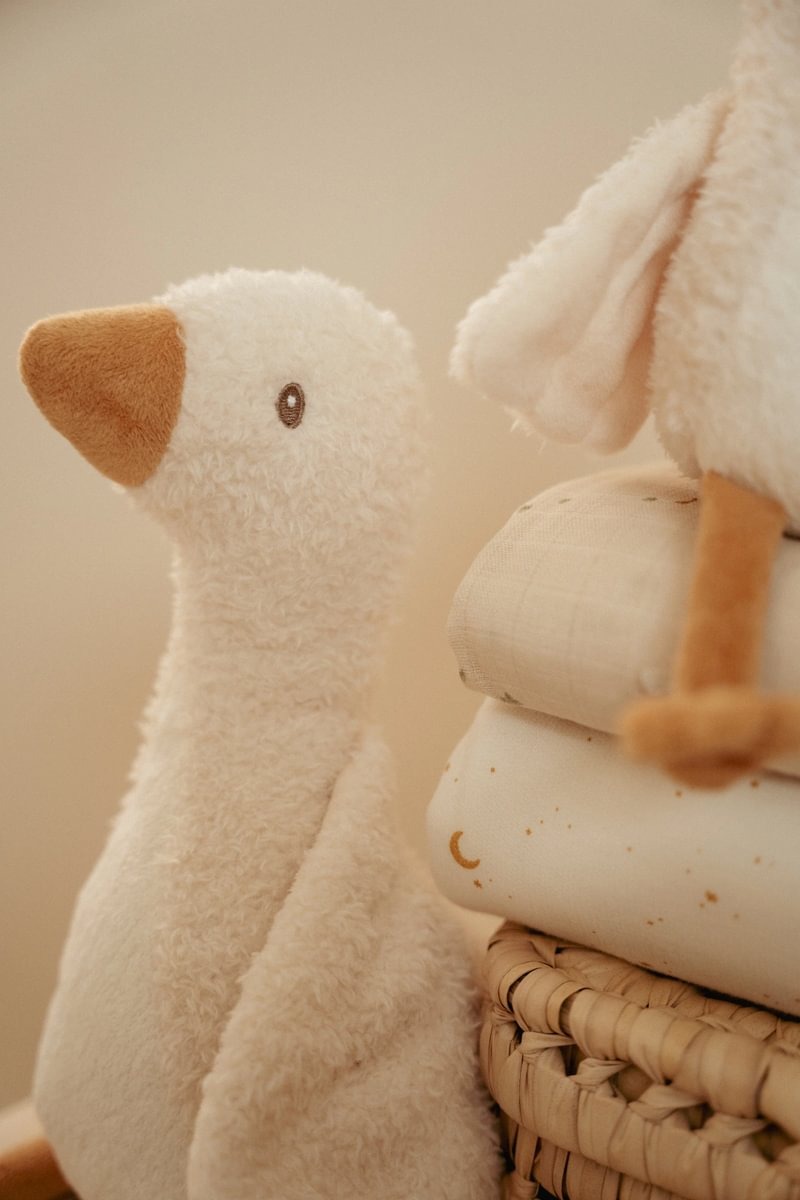 Pelúcia de ganso creme e bico castanho ao lado de mantas claras sobre cesto de vime