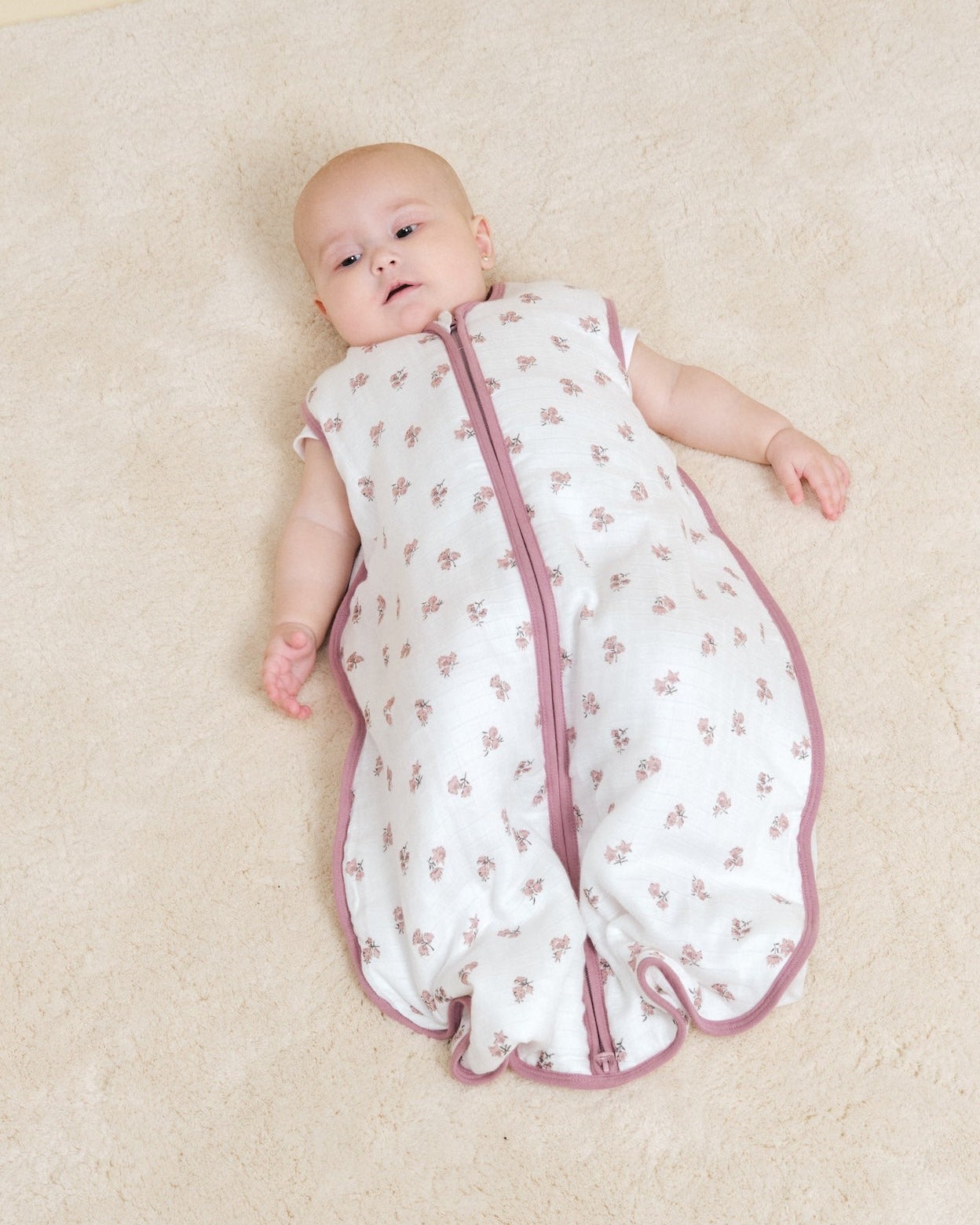 Saco de dormir para bebé branco com flores cor-de-rosa e fecho rosa.