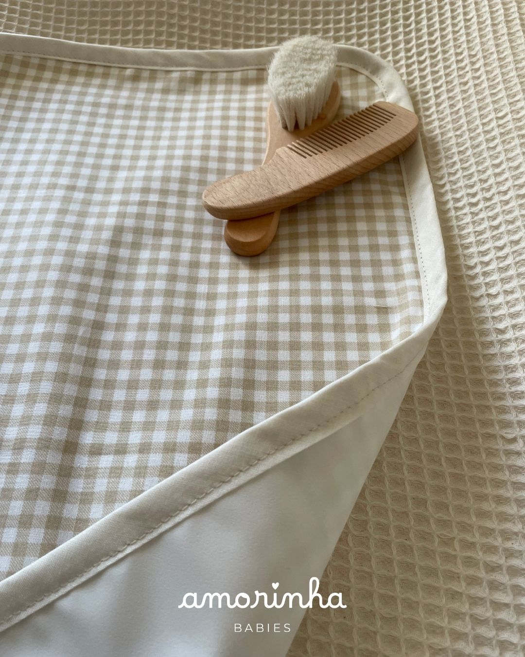 Tapete de bebé bege xadrez com escova e pente de madeira sobre tecido branco texturizado