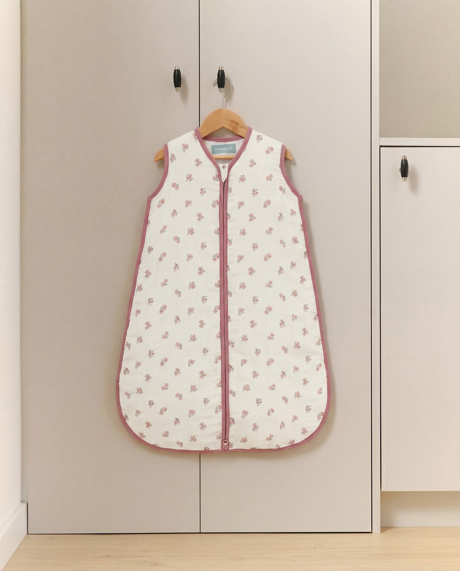 Saco de dormir para bebé branco com flores cor-de-rosa pendurado num armário cinzento