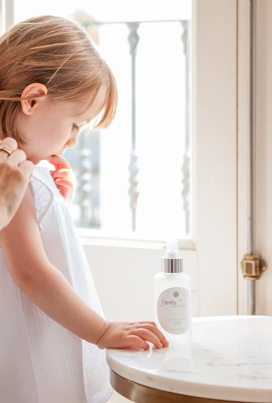 Garoto com vestido branco ao lado de garrafa branca com tampa prateada em mesa de mármore