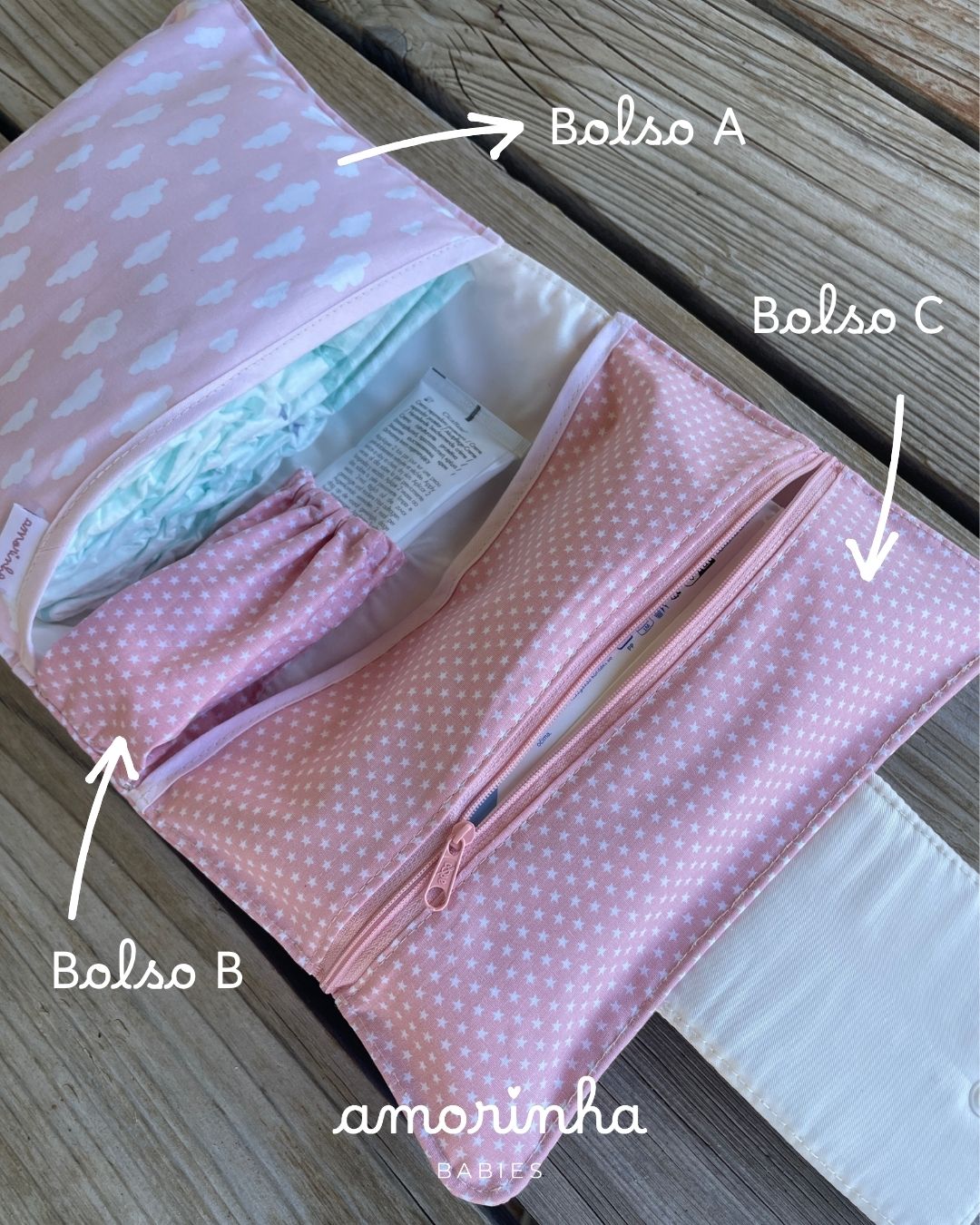 Organizador rosa para bebé com padrões de nuvens e estrelas, três bolsos etiquetados e logo AMORINHA BABIES.