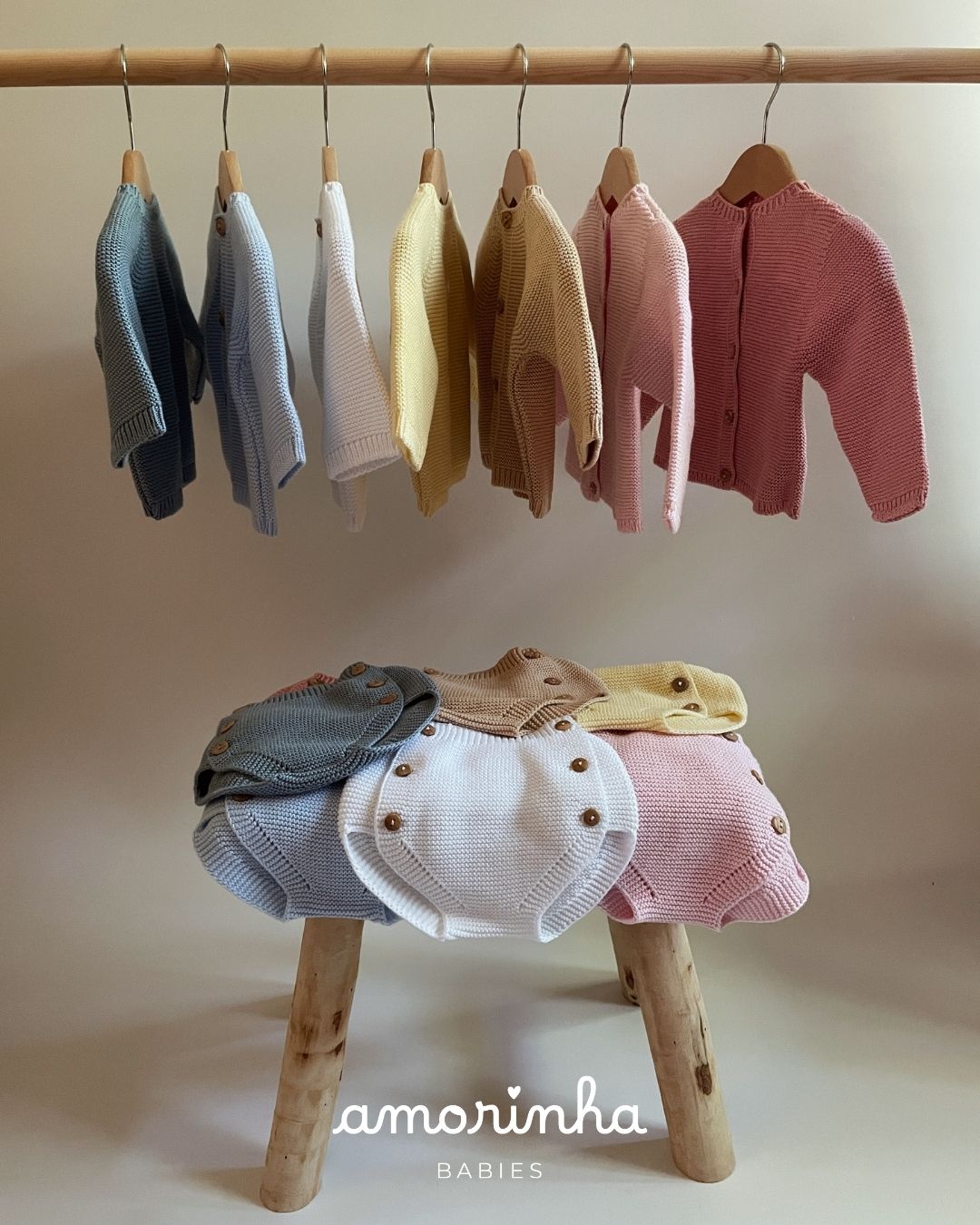 Roupas de bebé em malha coloridas penduradas e dobradas com texto amorinha BABIES