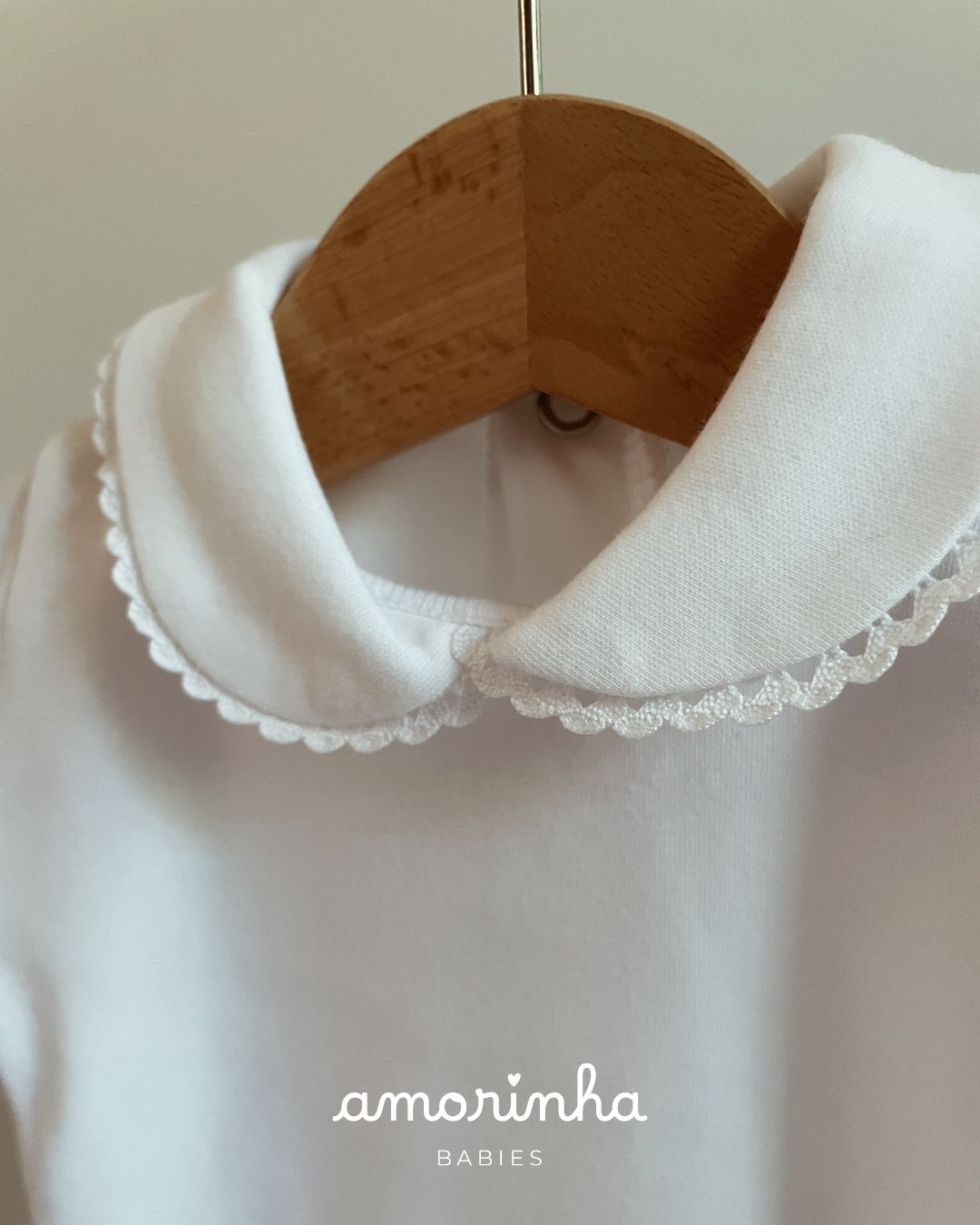 Roupa branca para bebés com gola redonda bordada em cabide de madeira