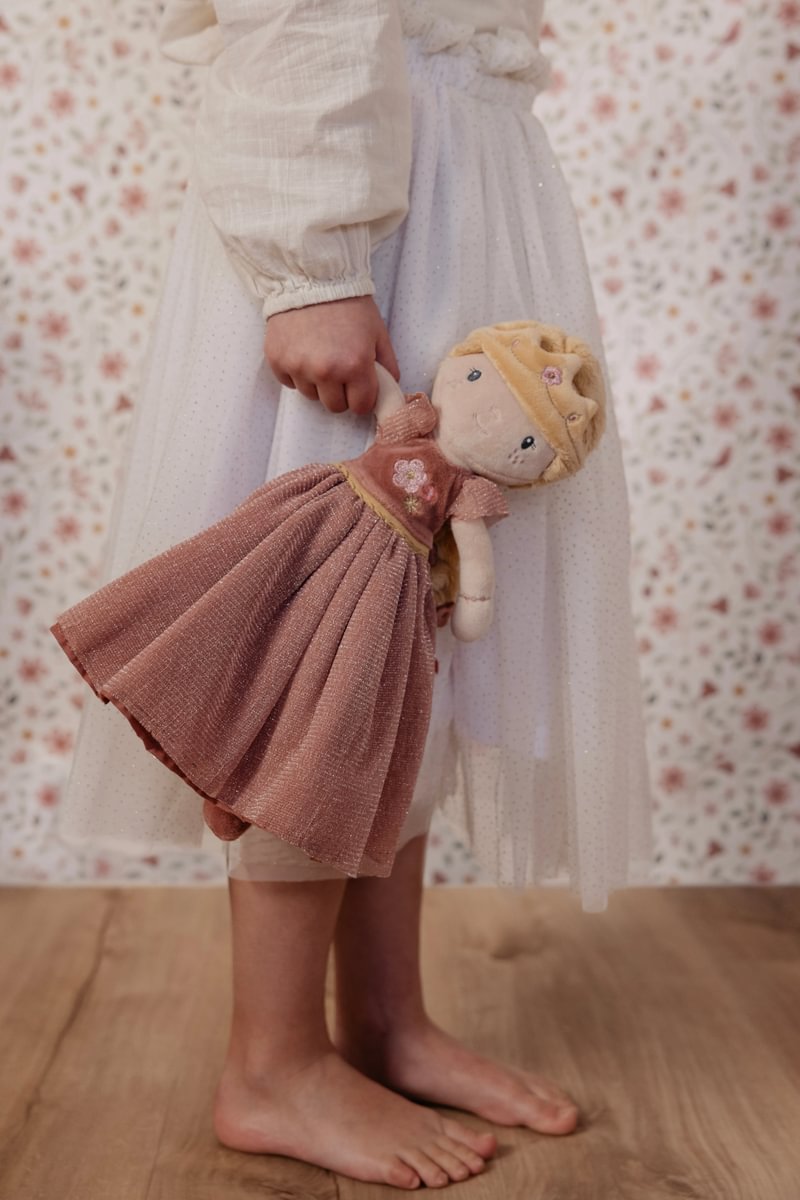Boneca de pano com vestido rosa segurada por criança de vestido branco