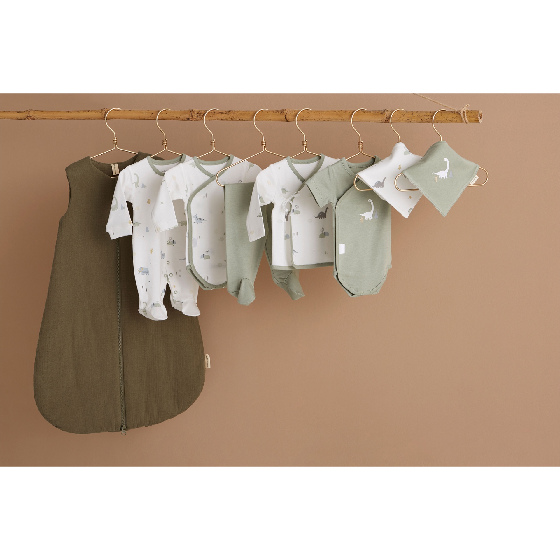 Roupa de bebé em verde-oliva e branco com padrões de dinossauros pendurada numa vara de madeira.
