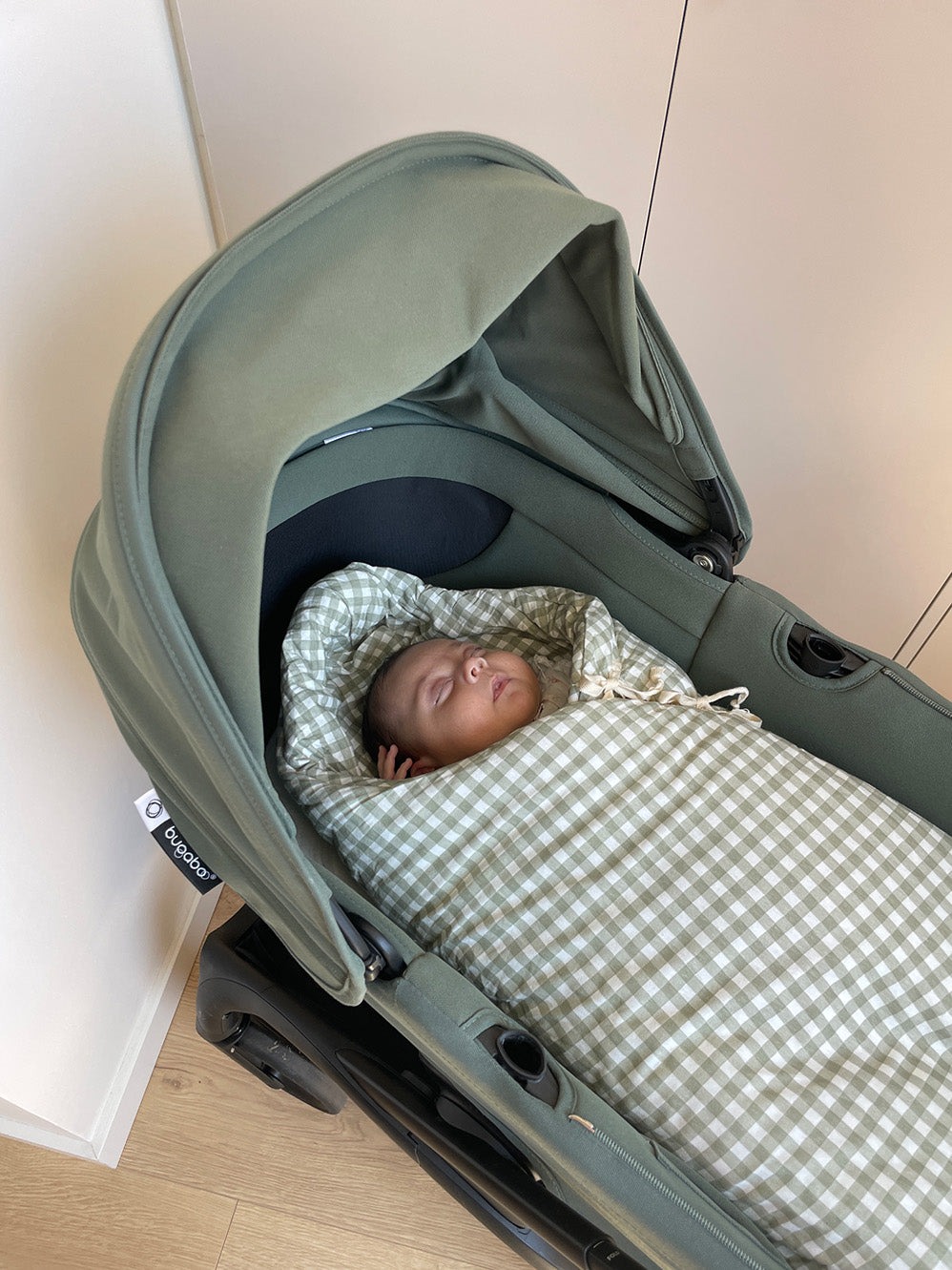 Carrinho de bebé verde com bebé enrolado em saco de dormir xadrez